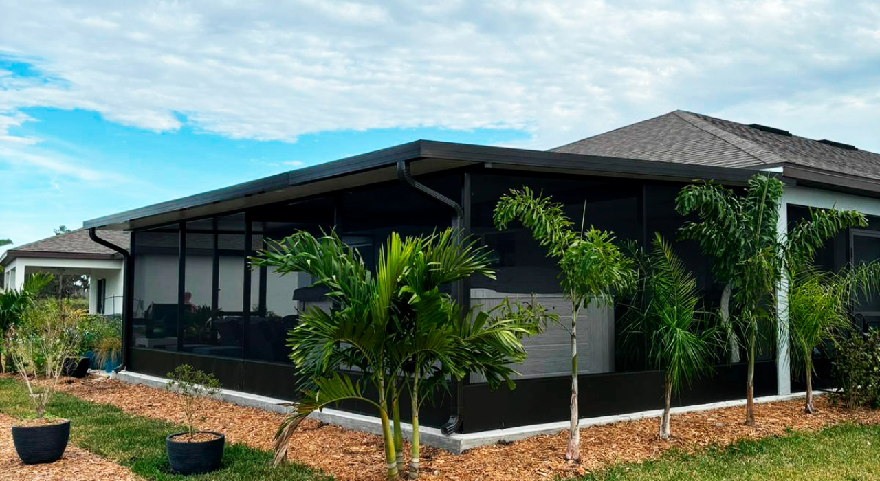 A large, modern stone patio under a protective mesh enclosure, perfect for comparing a lanai vs screened porch design.