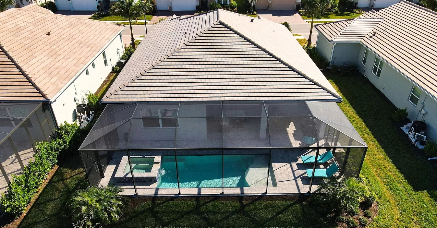 A sparkling backyard pool protected by a tall mesh structure, demonstrating the importance of how to clean pool screen enclosure.