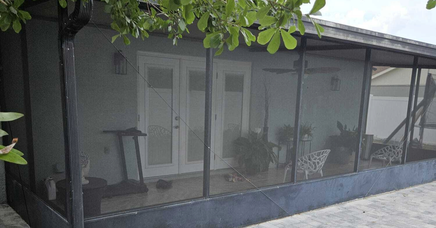 A long screened-in patio with a solid kickplate bordered by stone, showcasing distinct lanai enclosure ideas.